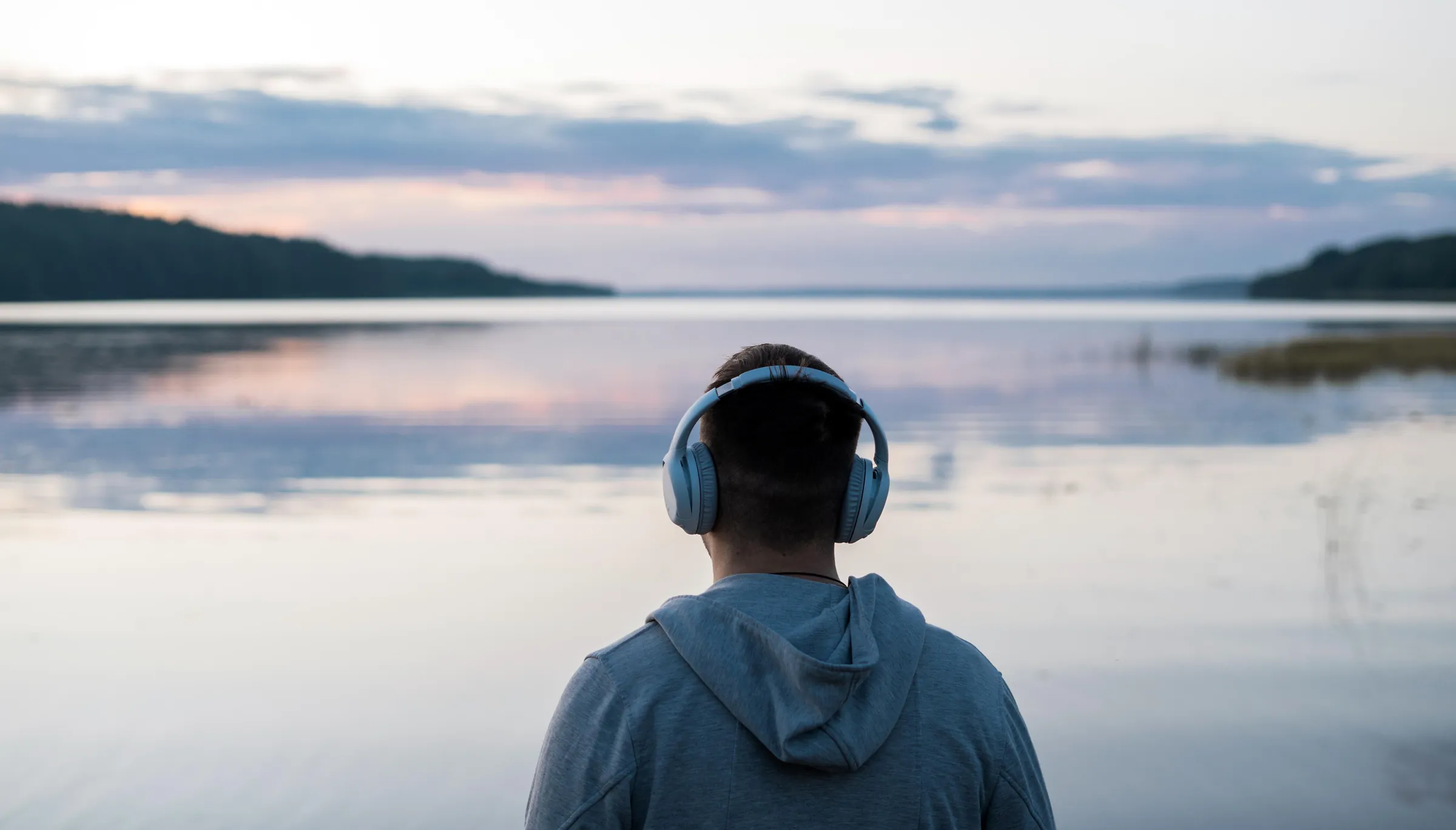 Listener at a lakeside at dusk wearing headphones
